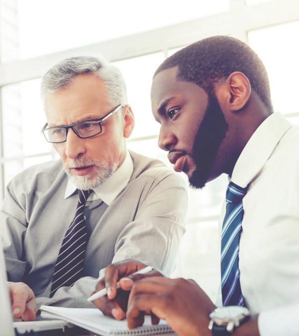 Concept for teamwork and knowledge transfer Photo of aged businessman and his colleague. Businessmen working in office with big window. Men using laptop